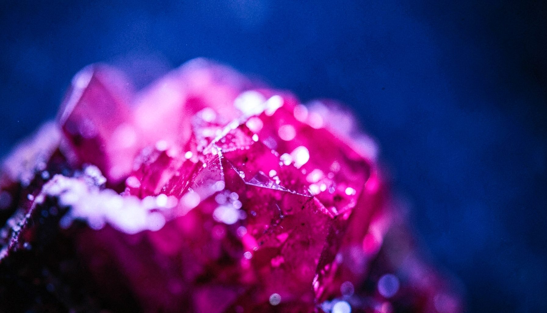 Close up of a glowing magenta crystal surface against a deep blue background, soft bokeh, candid documentary style photograph